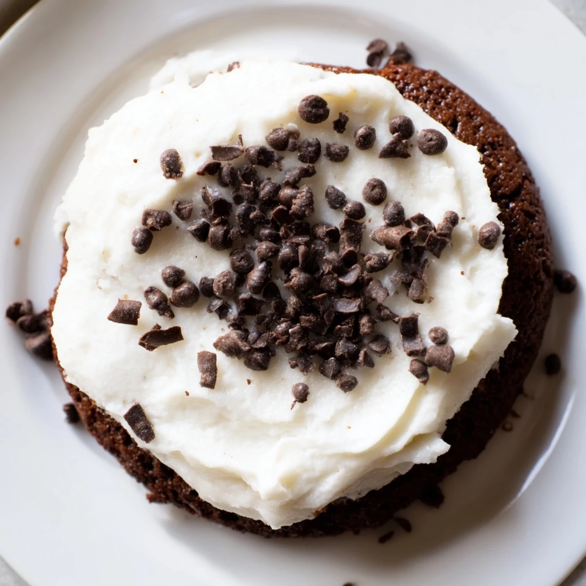 Large bakery-style chocolate cookies with luscious vanilla frosting and sprinkles on a white plate.