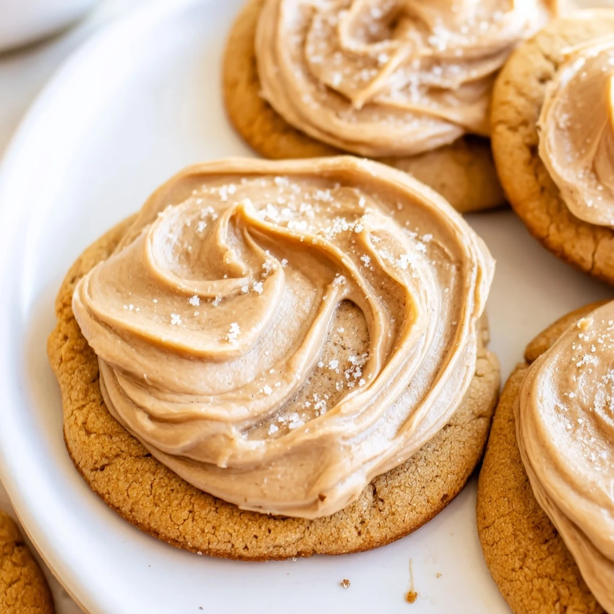 Overhead view of Holiday Glow Caramel Frost Vegan Cookies arranged on a wooden board with chopped pecans and a glass of plant milk.