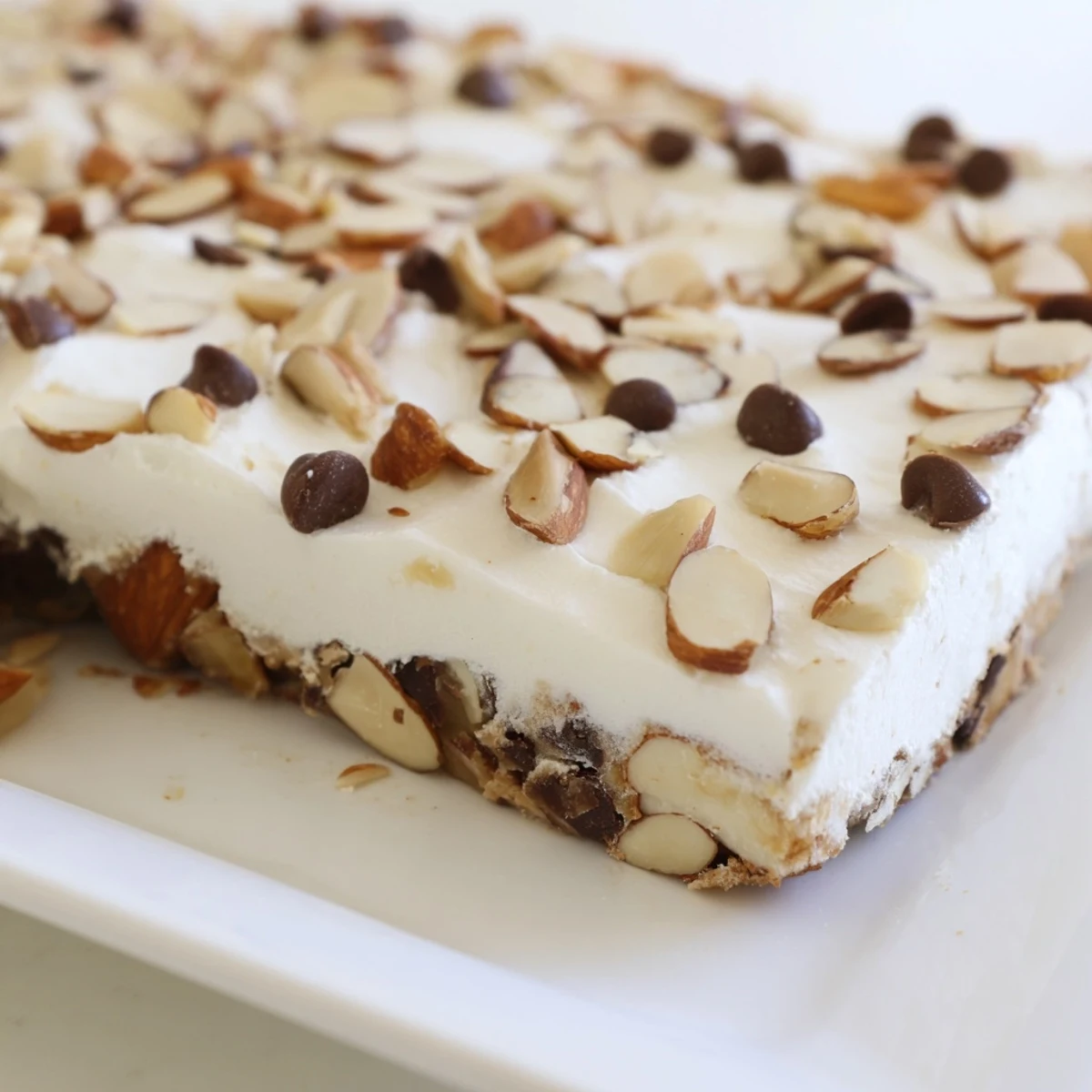 A single Frosted Delight Toasted Almond Chocolate Chip bar lifted from the pan, revealing a moist interior and a thick layer of creamy frosting, perfect for an afternoon treat.  