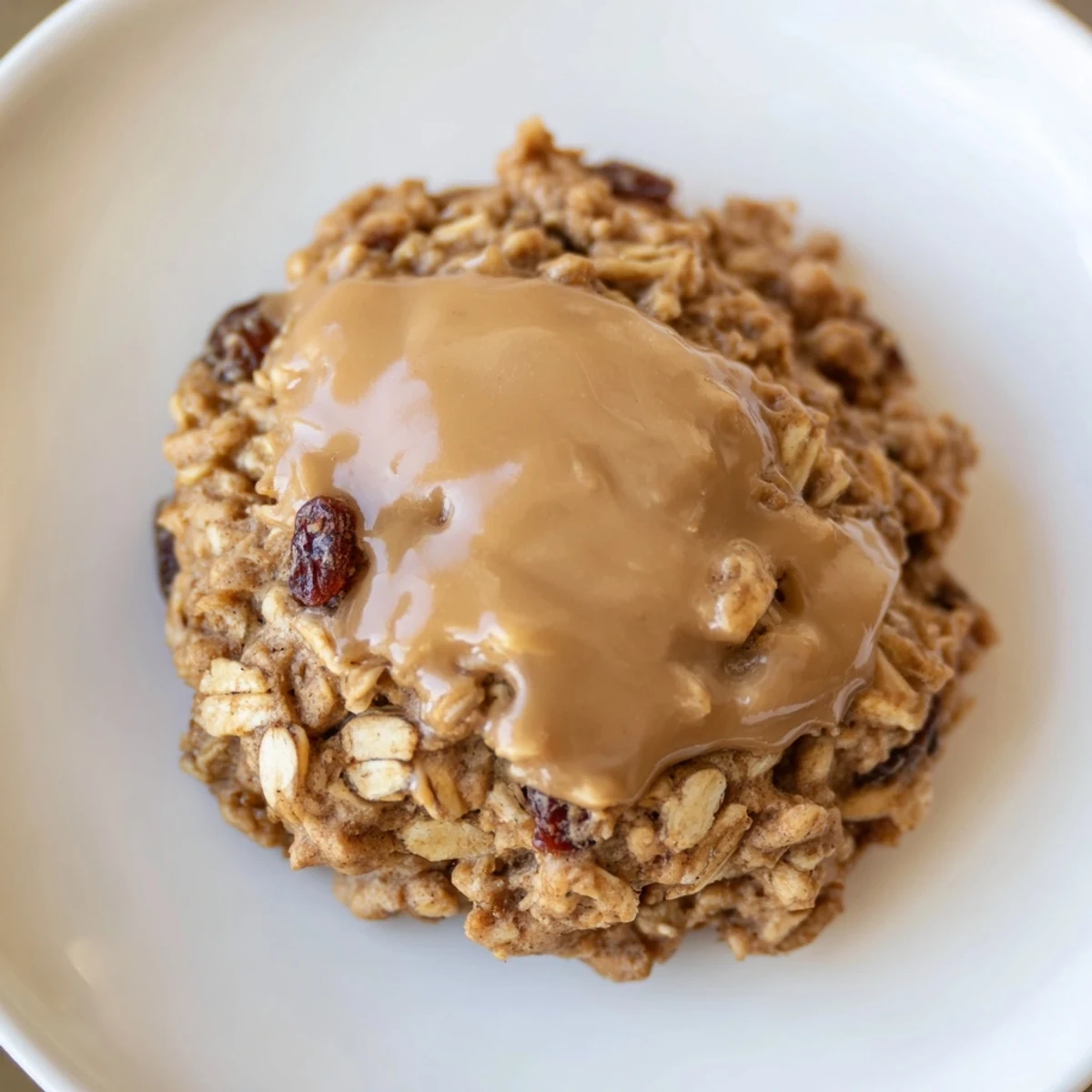 A close-up of Winter Warmth Caramel Frost Oatmeal Raisin cookies, with a glossy caramel glaze dripping over chewy oats and plump raisins.