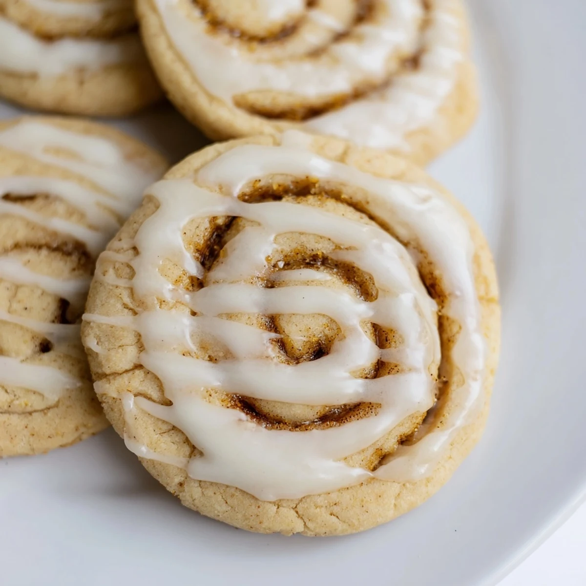 Freshly baked Cinnamon Roll Inspired Sugar Cookies arranged on a cooling rack with a bowl of vanilla glaze and cinnamon sticks nearby.