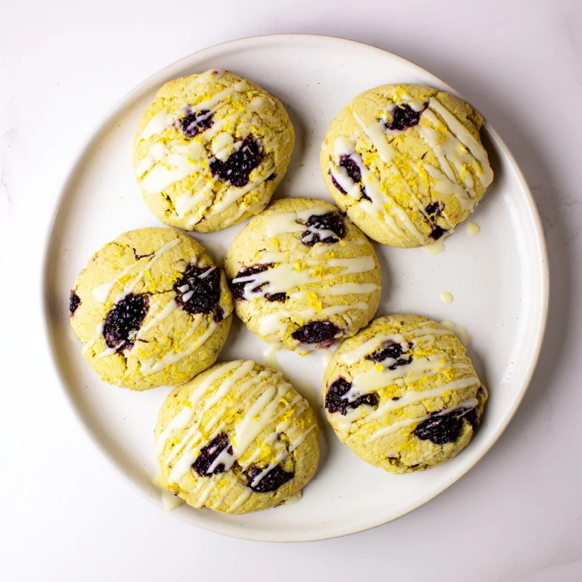 Golden-brown Vegan Blackberry Lemonade Cookies with a lemon glaze and fresh blackberry pieces on a rustic wooden table.