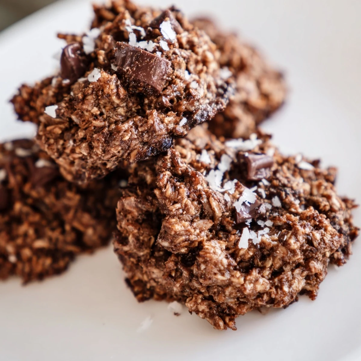Chewy keto mocha coconut cookies stacked on a white plate with chocolate chunks visible