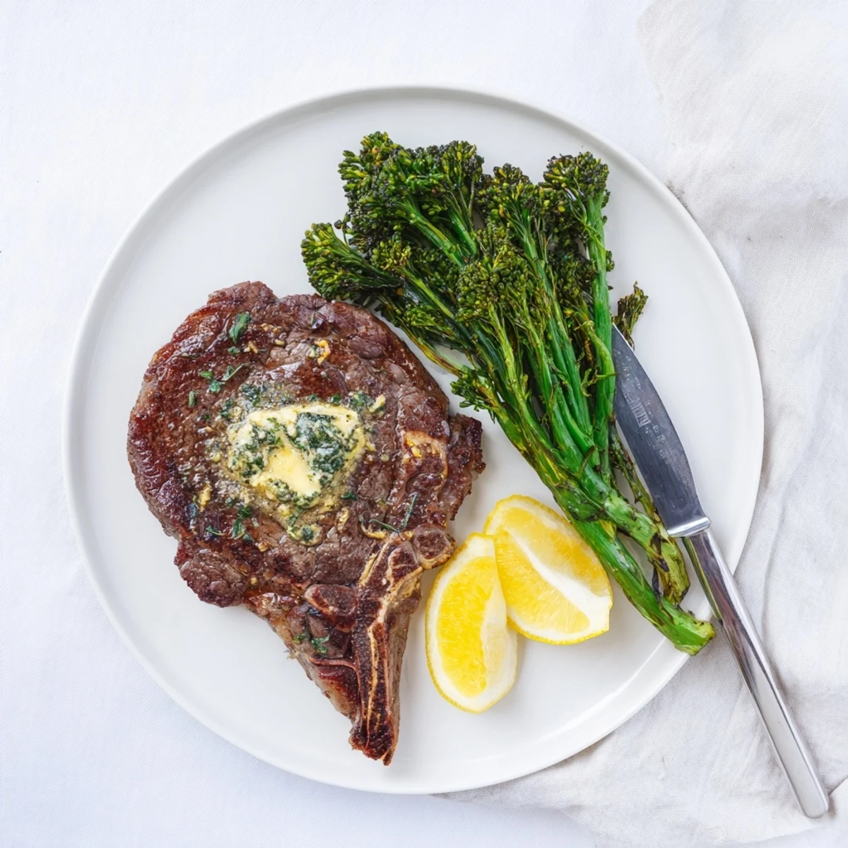 Juicy ribeye steak basted with garlic butter herbs alongside crisp tender roasted broccolini and lemon