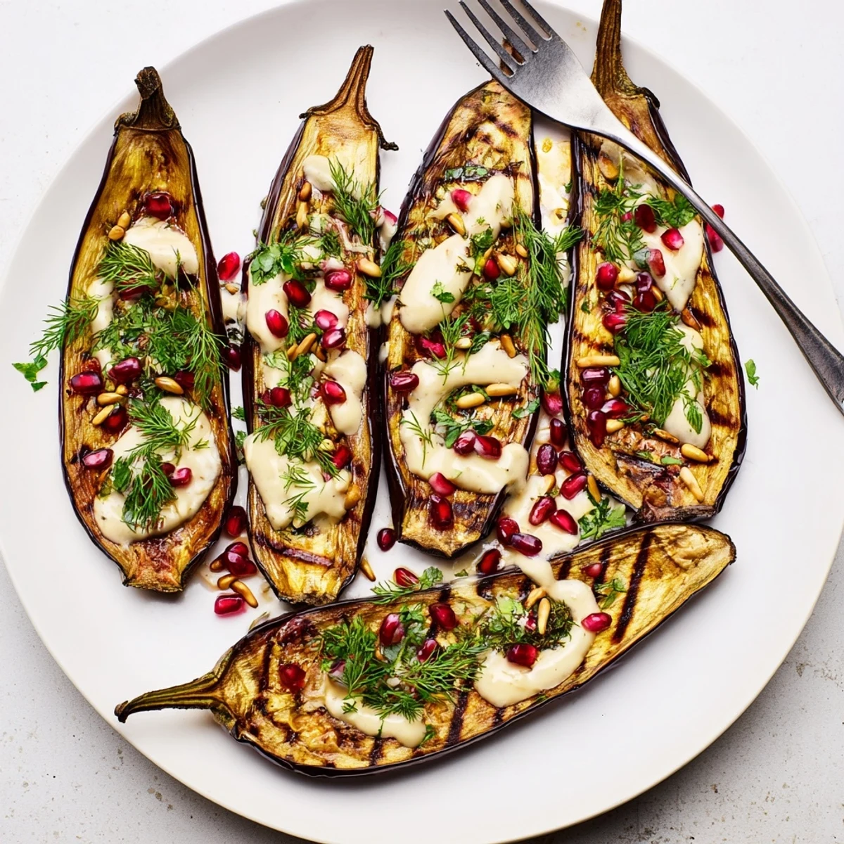 Golden roasted eggplant halves drizzled with creamy lemon herb tahini sauce and fresh herbs