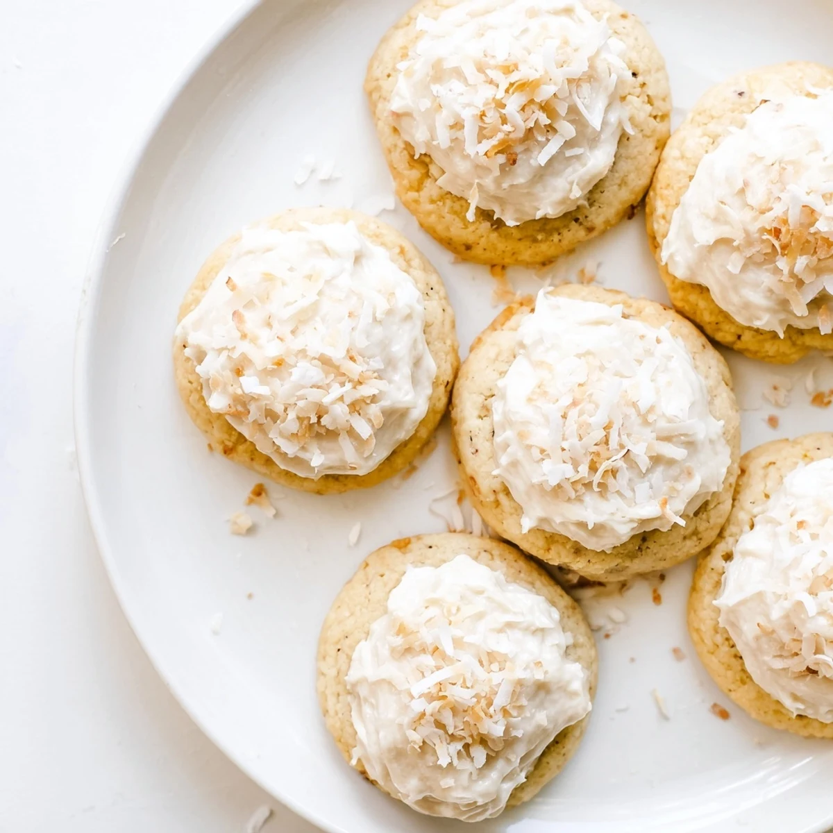 Golden vegan pineapple coconut cream sugar cookies topped with fluffy white frosting and coconut sprinkles