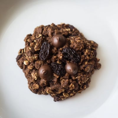 Two Warmth Cocoa Burst Oatmeal Raisin cookies with cracked tops and cinnamon spice on a wooden board.