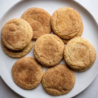 Gluten-Free Churro Sugar Cookies stacked on a wooden cutting board, showing a soft, chewy texture and crackled cinnamon tops.