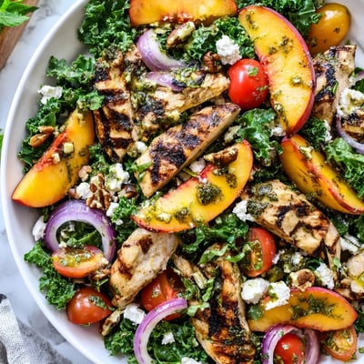 Vibrant Grilled Peach and Kale Chicken Salad drizzled with refreshing mint-basil dressing on a platter